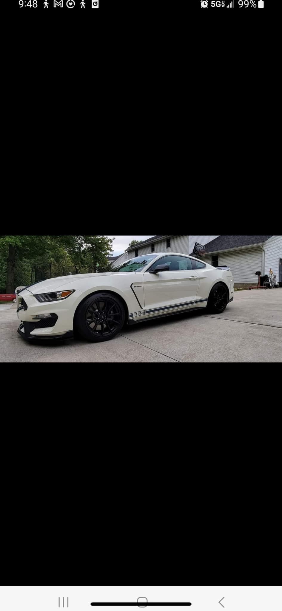 A white mustang is parked in a parking lot in front of a house.