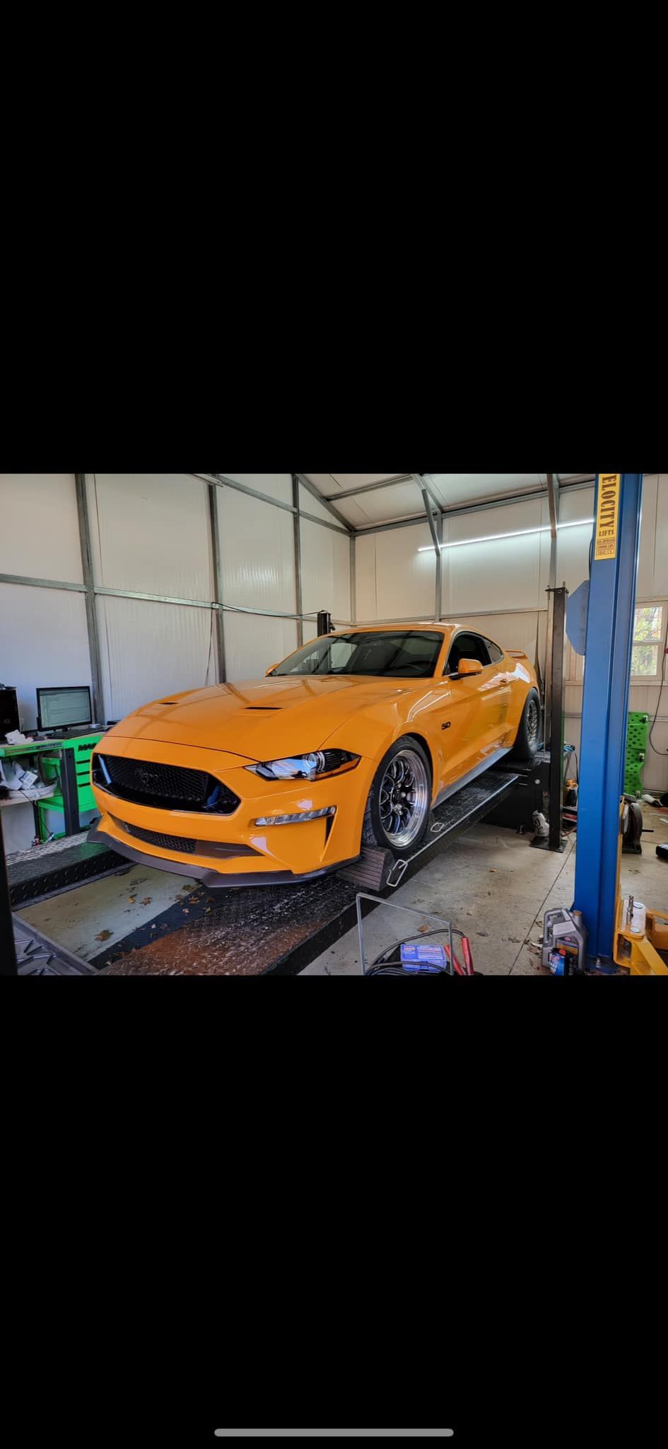 A yellow mustang is parked on a lift in a garage.