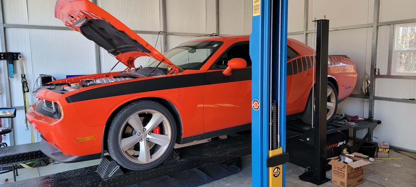 An orange dodge challenger is parked on a lift in a garage.