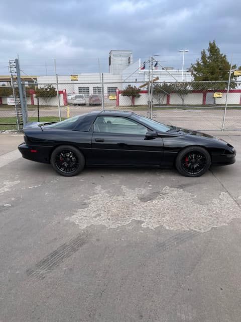 A black car is parked in a parking lot in front of a building