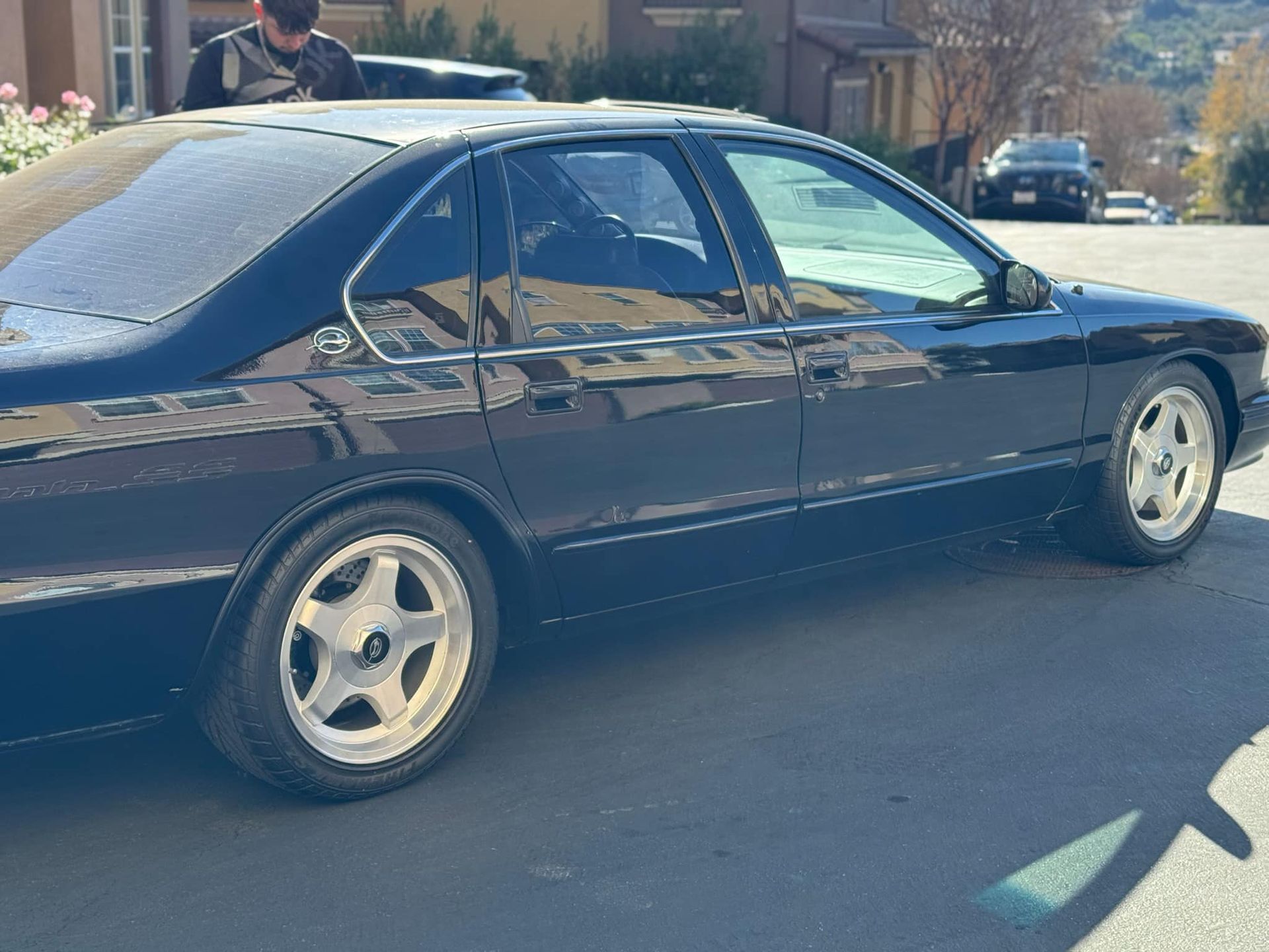 A man is standing next to a black car in a parking lot.