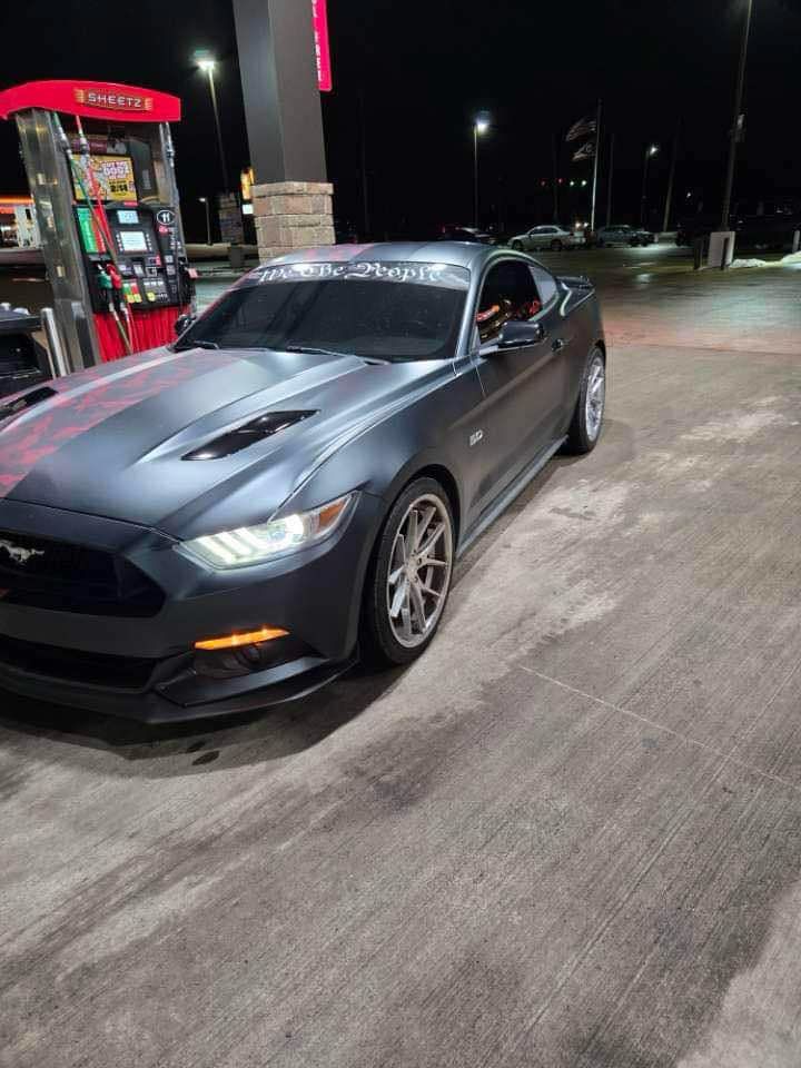 A black mustang is parked in a gas station at night.