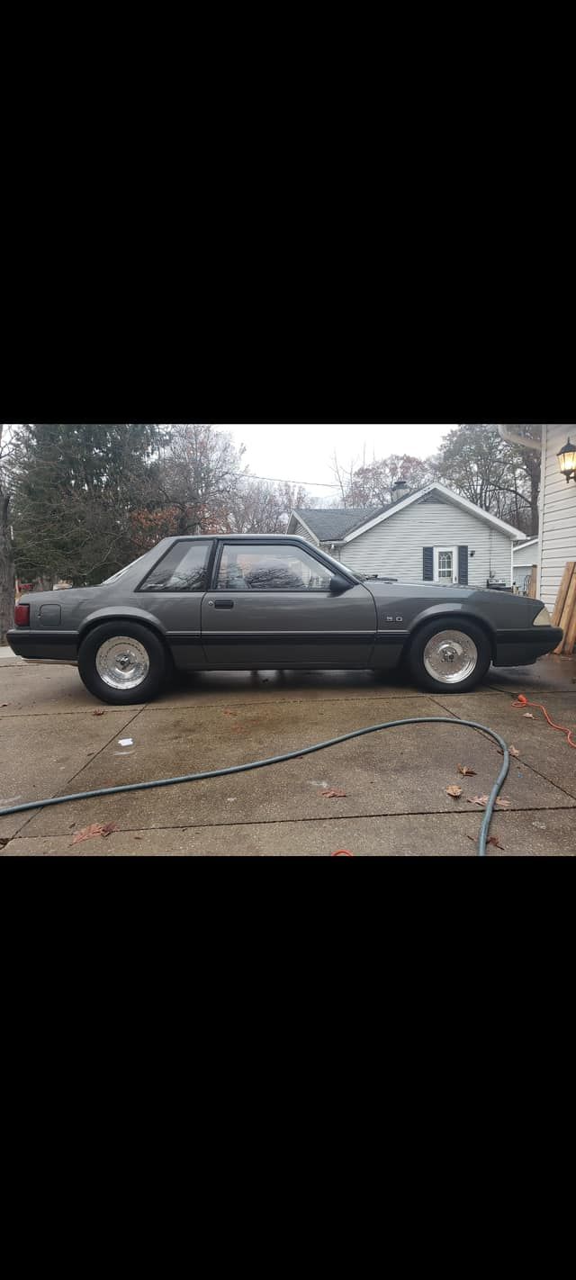 A gray mustang is parked in a driveway in front of a house.