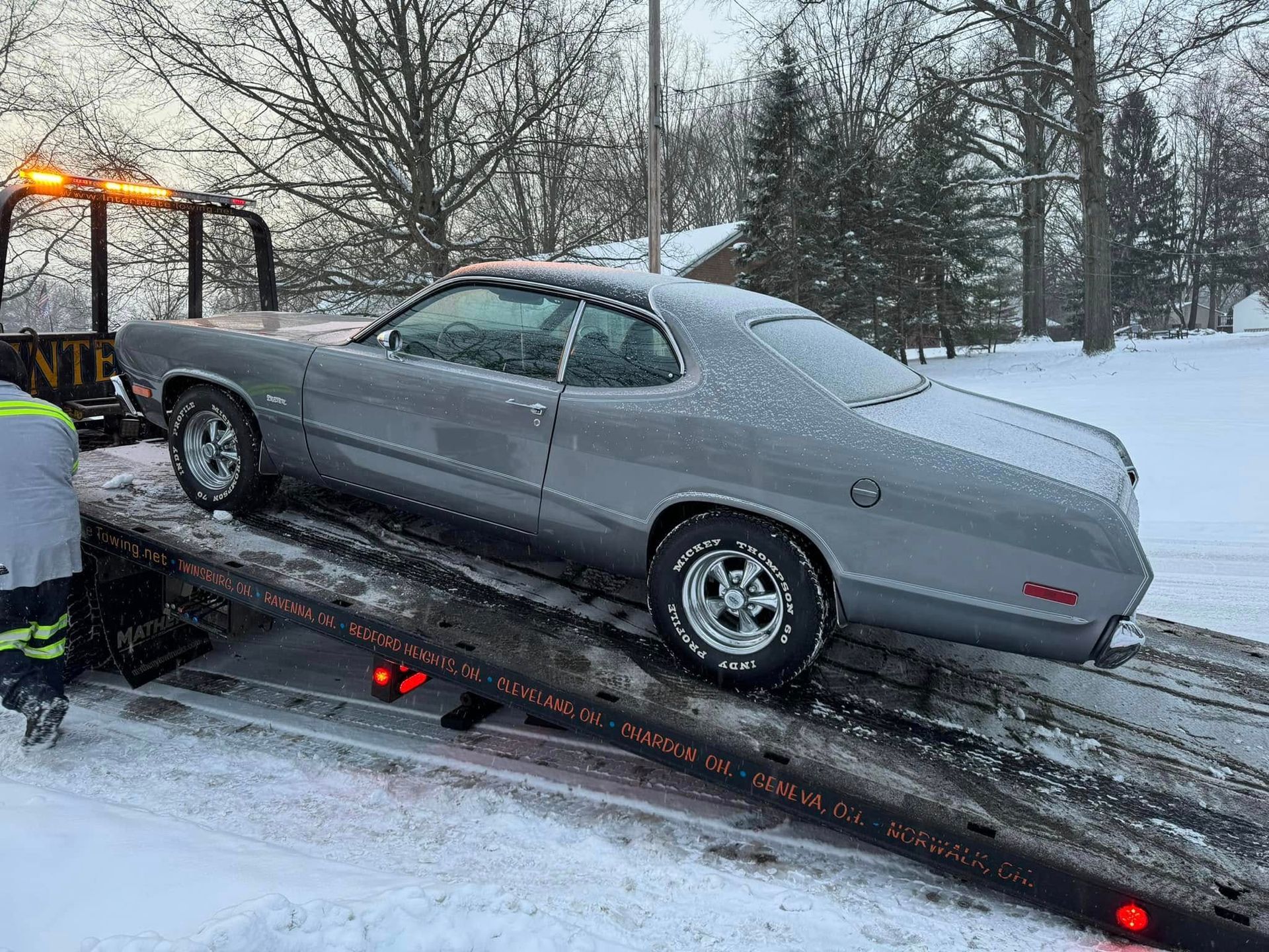 A silver car is being towed by a tow truck in the snow.