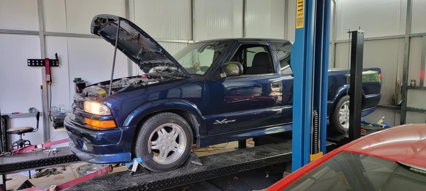 A blue truck with its hood up is on a lift in a garage.