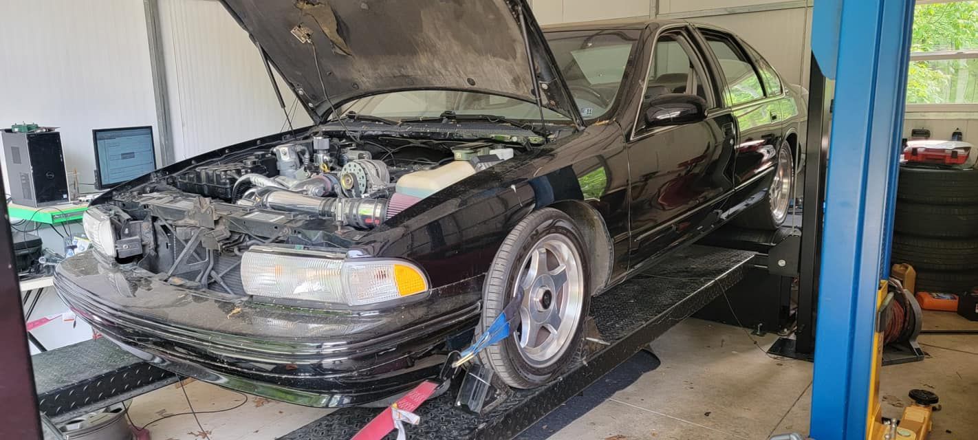 A black car with the hood up is on a lift in a garage.