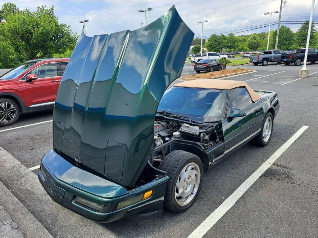 A green corvette convertible with the hood up is parked in a parking lot.