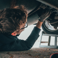 A man wearing glasses is working under a car