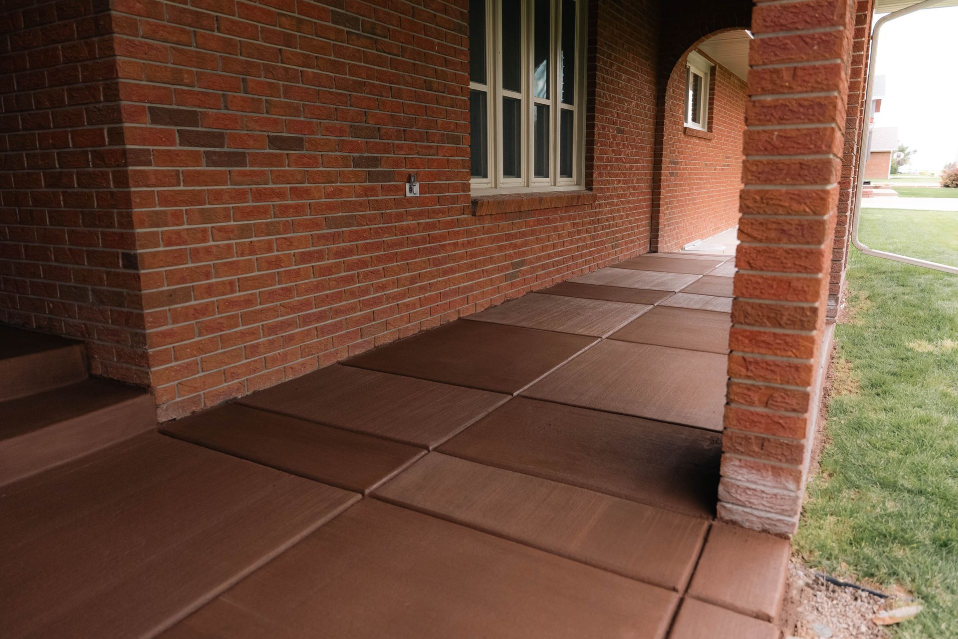 Brick porch with brown concrete tiles; brick pillars and wall; window visible.