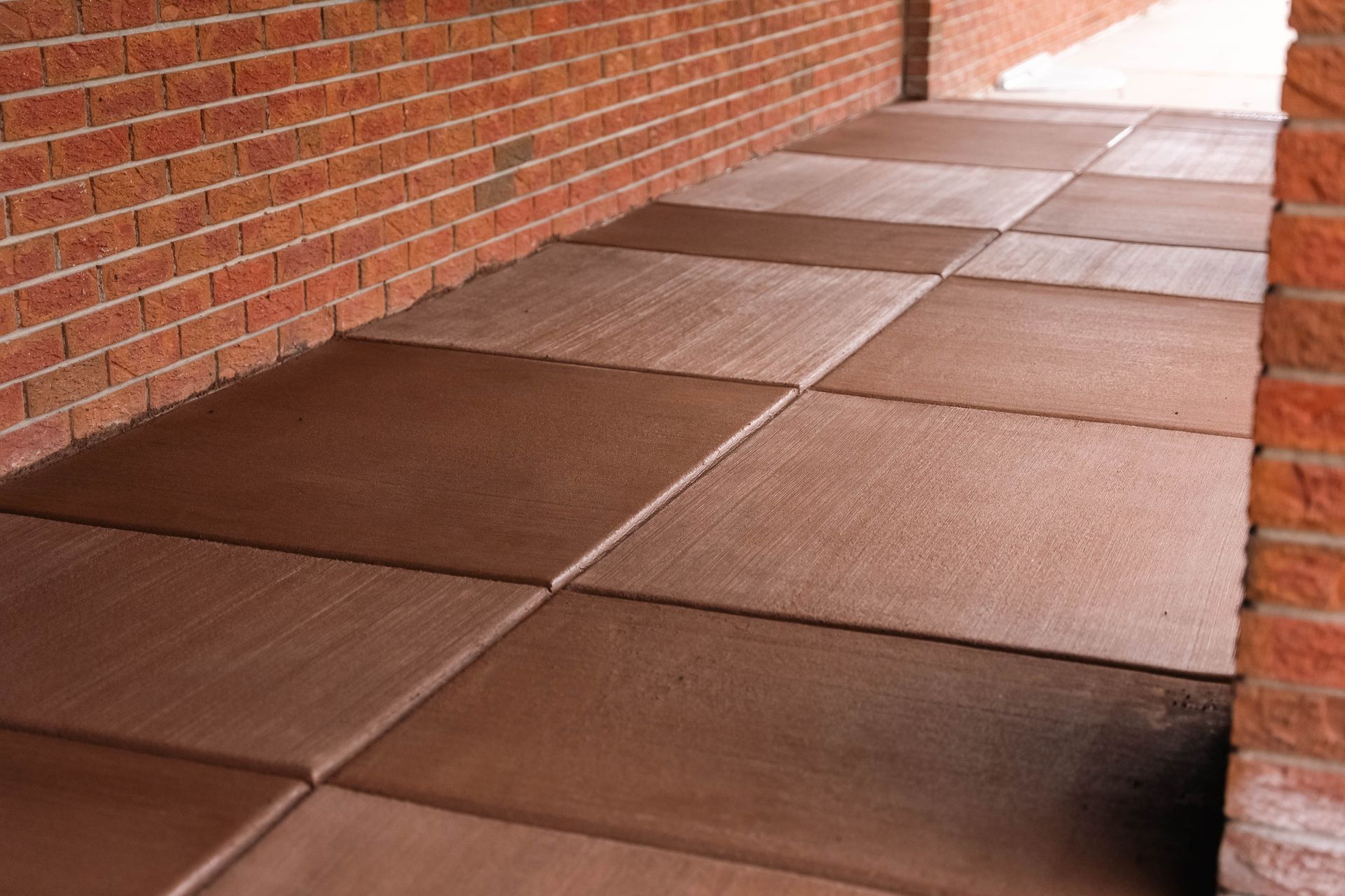 Brown tiled walkway bordered by a red brick wall, leading into a covered area.