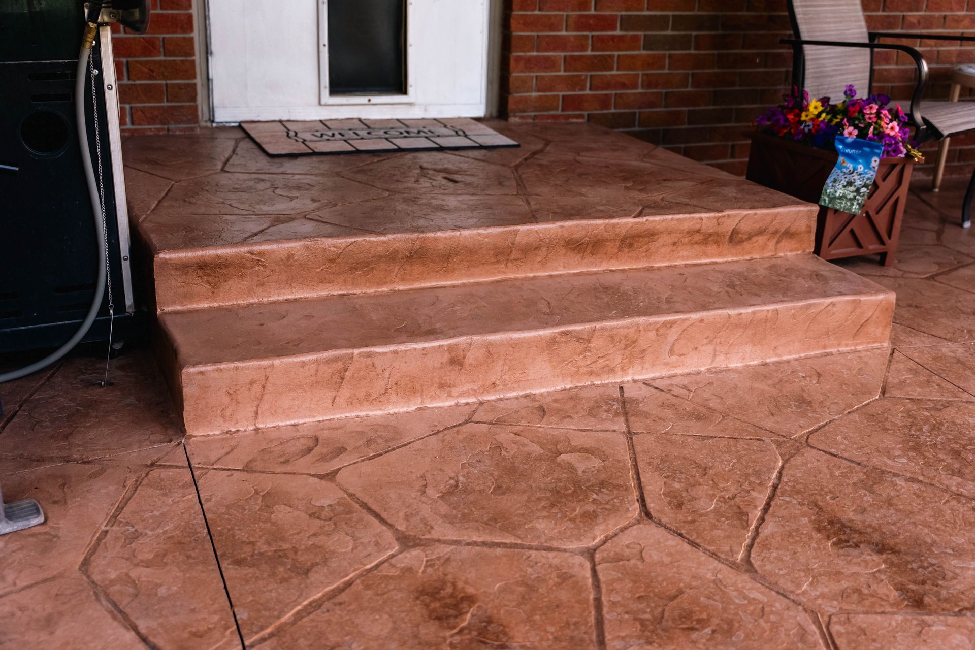 Brown stone stamped concrete steps leading to a white door with a small window.