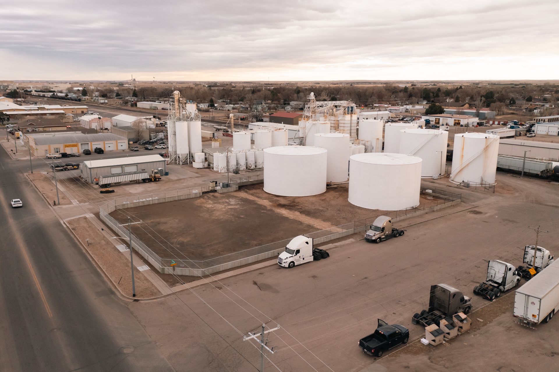 Aerial view of an industrial facility with white storage tanks, trucks, and a cloudy sky.