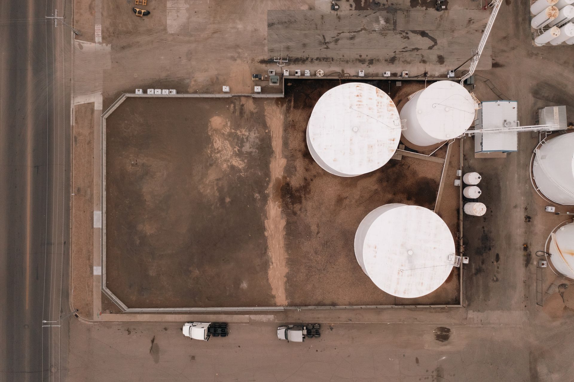 Aerial view of industrial site with white storage tanks and trucks parked near a road.