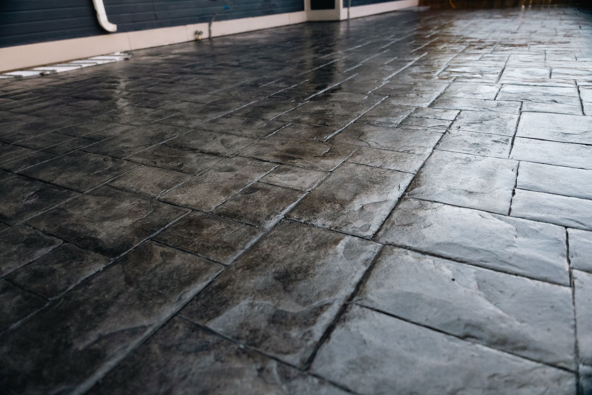 Wet, gray stamped concrete patio. Brick pattern, reflective surface, near a dark building.
