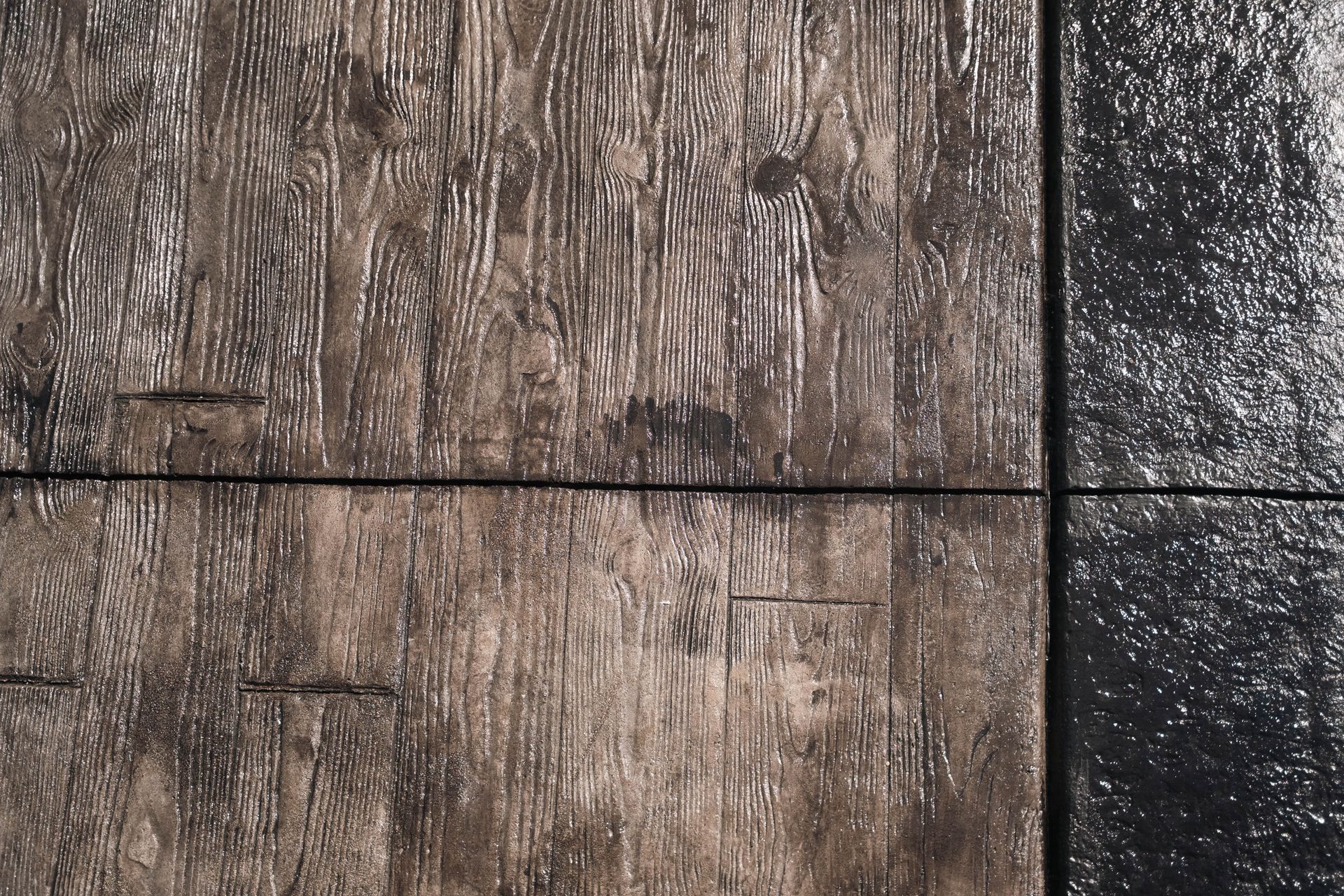Close-up of weathered wood-look concrete tiles with a contrasting glossy black tile.