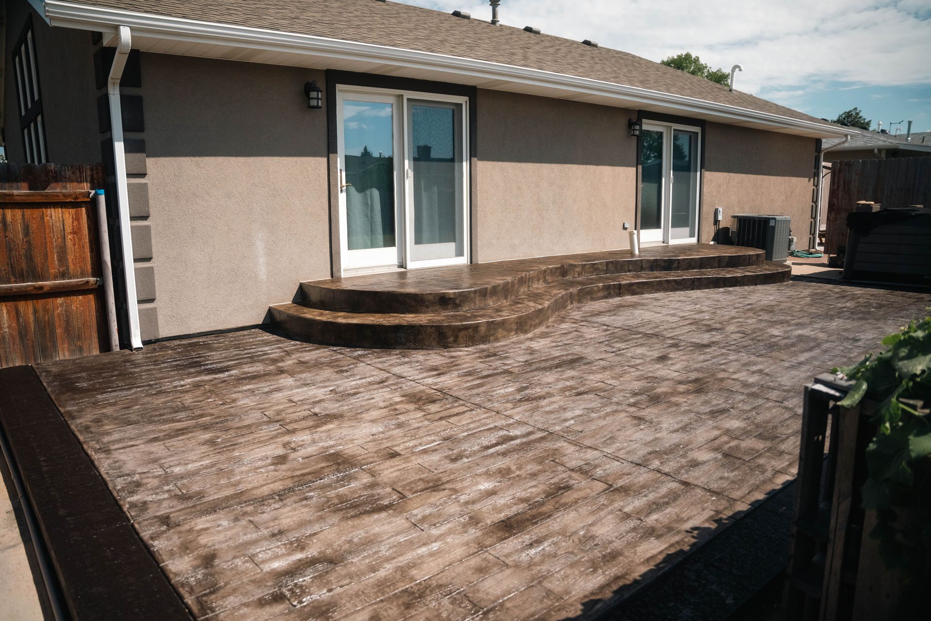Concrete patio with textured surface and steps leading to a house with sliding glass doors.
