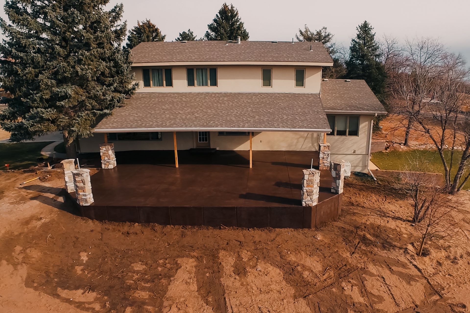 Two-story house with a large, dark brown deck. Stone pillars support the deck's roof.