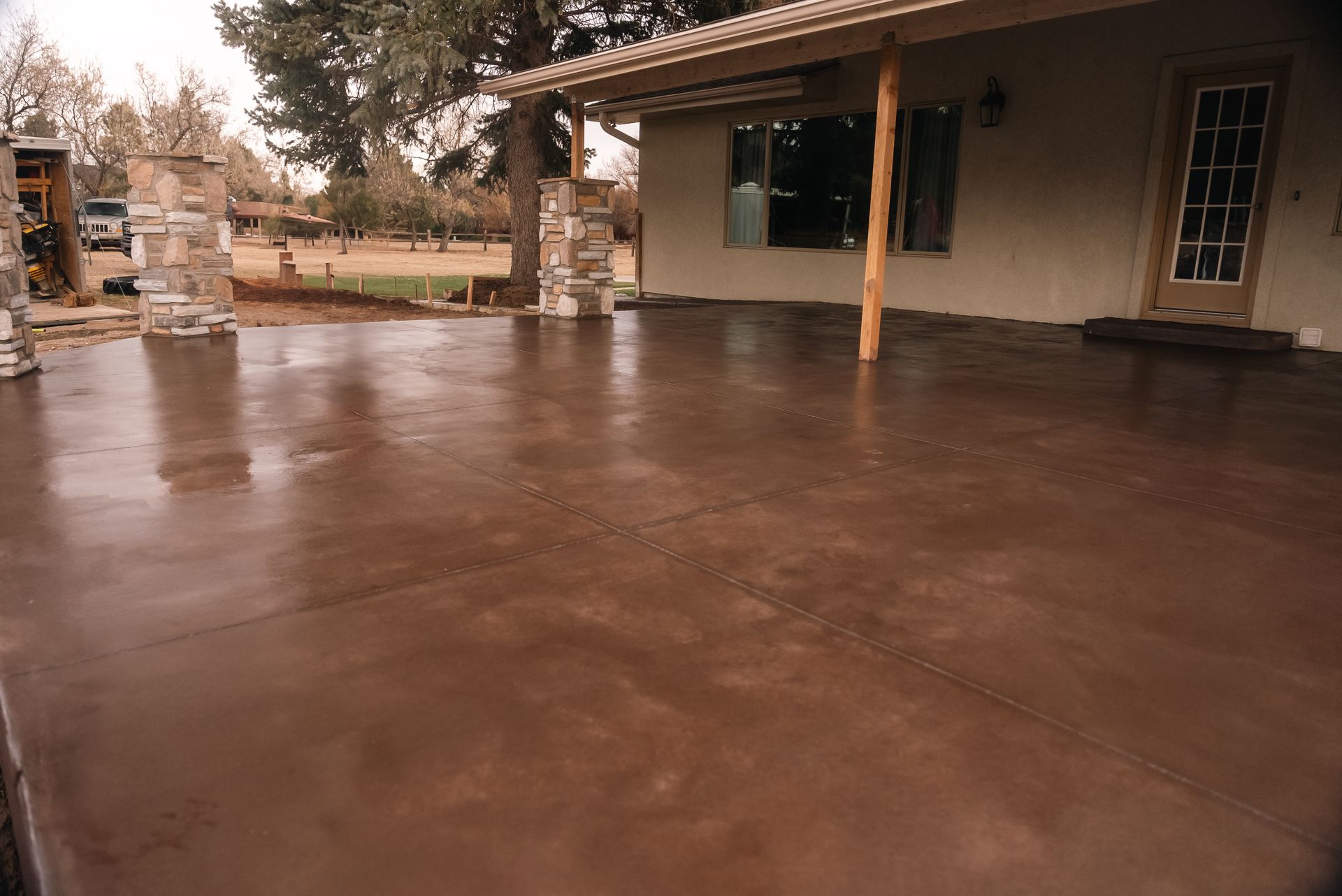 Brown concrete patio with a covered porch and stone columns.