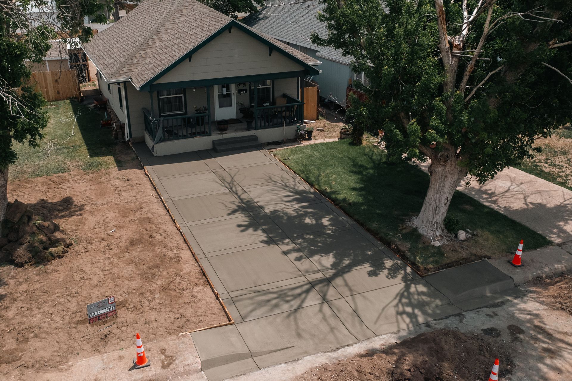 Aerial view of a house with a newly poured concrete driveway and front sidewalk. Orange traffic cones present.