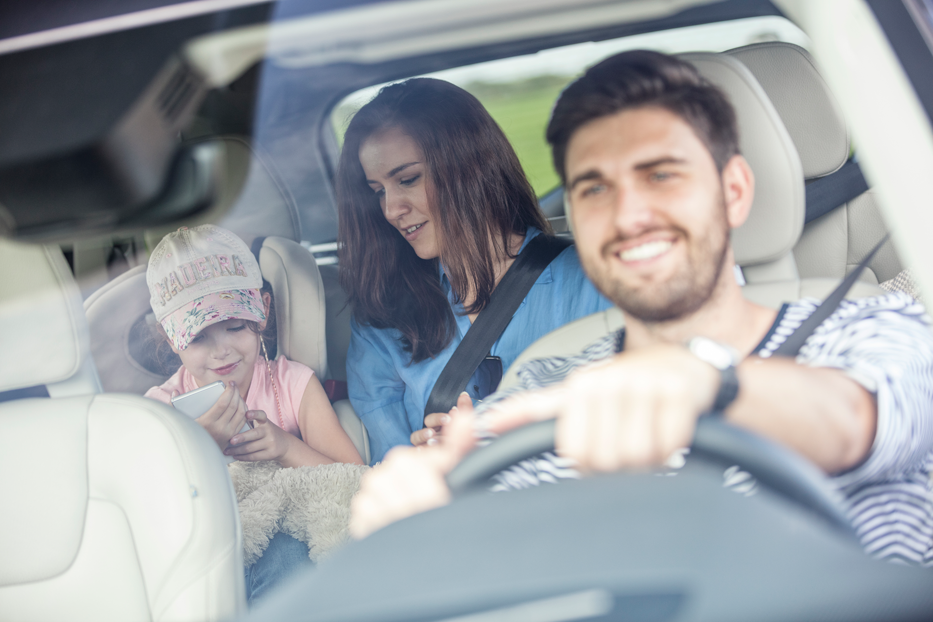 Family in a car. Man driving smiles, woman and child in back.
