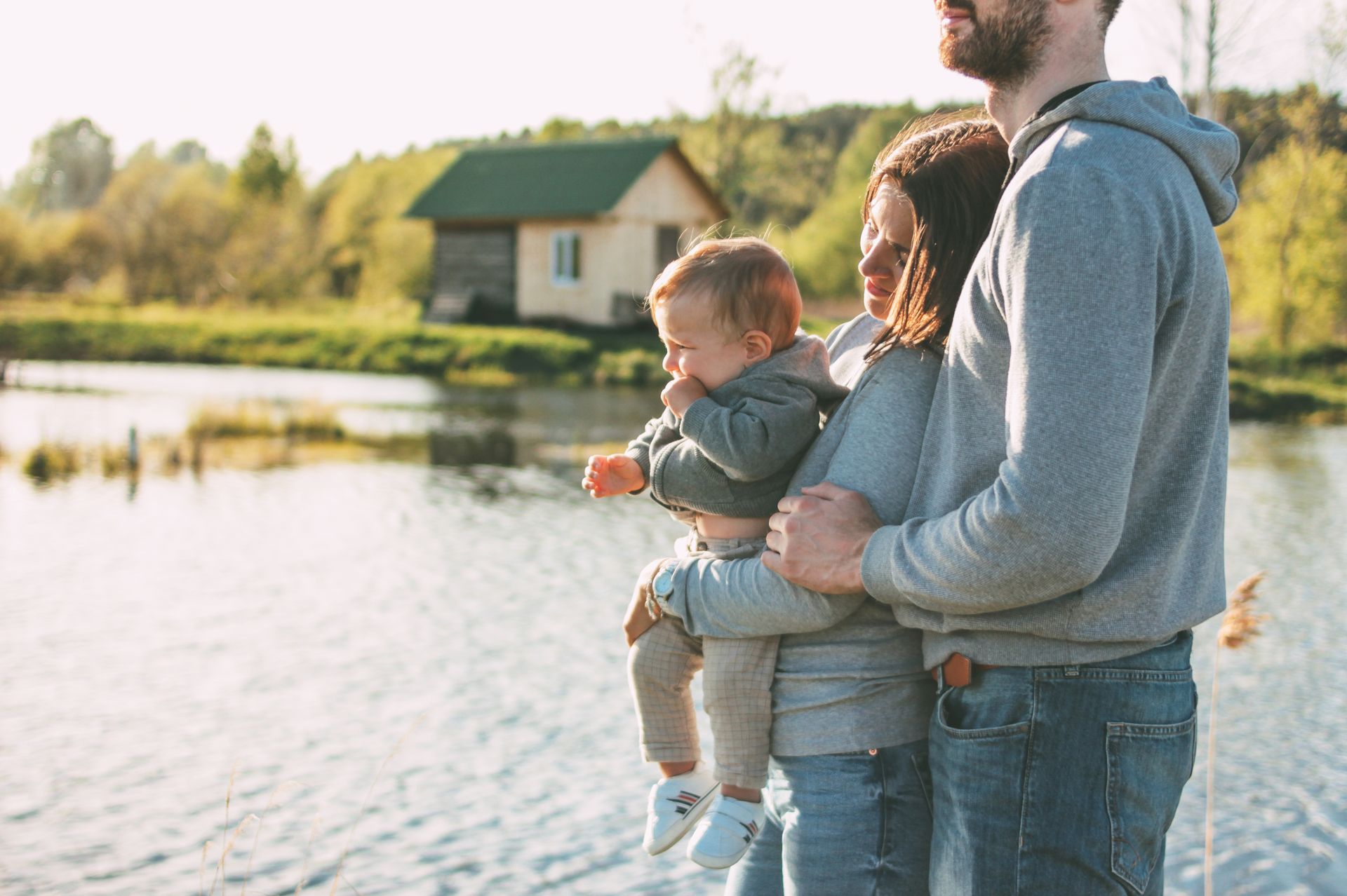 Family by a lake, the mother holding a child, the father standing next to them.