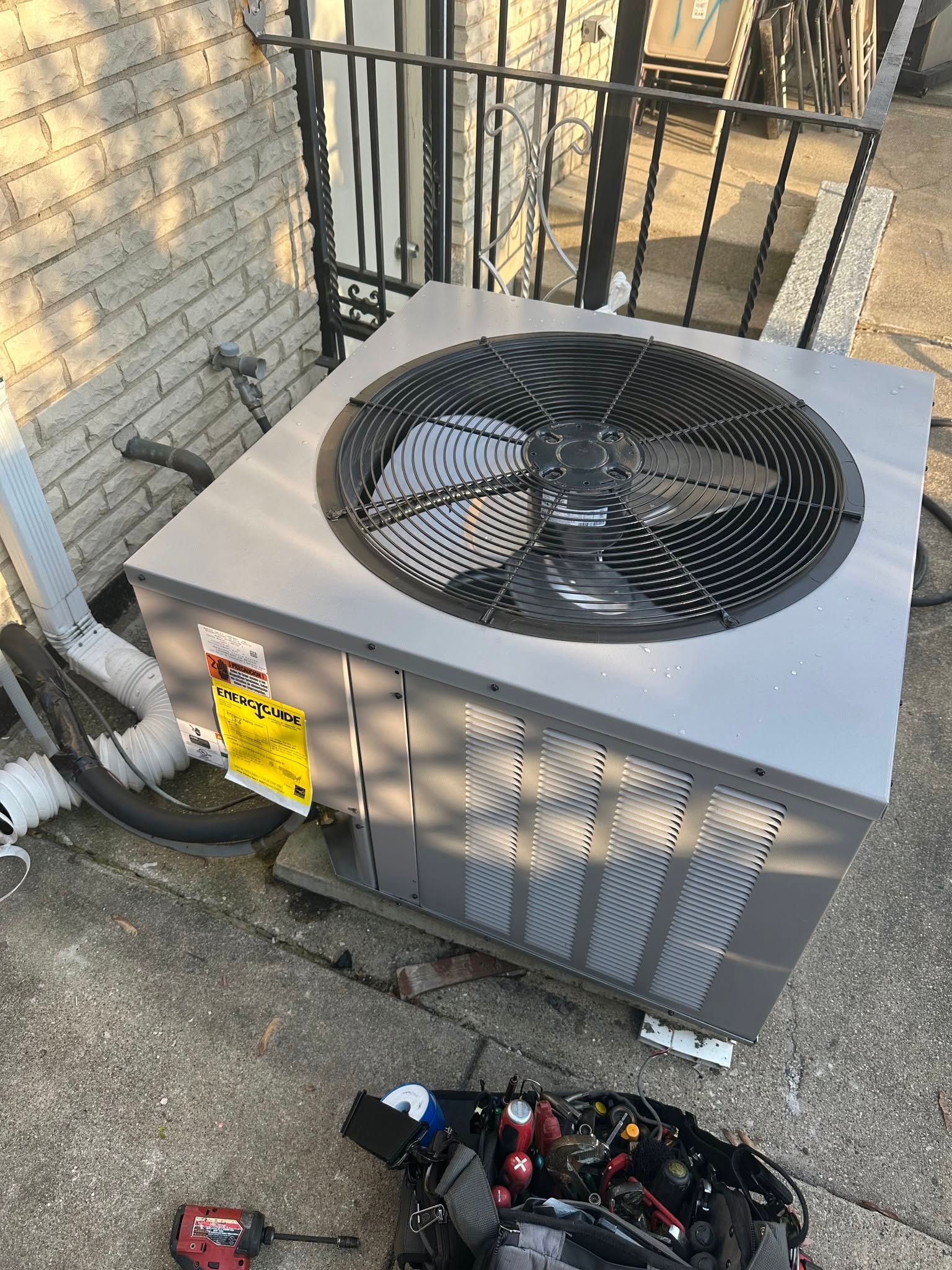 Outdoor HVAC unit with a top fan beside a brick wall and scattered tools on the ground