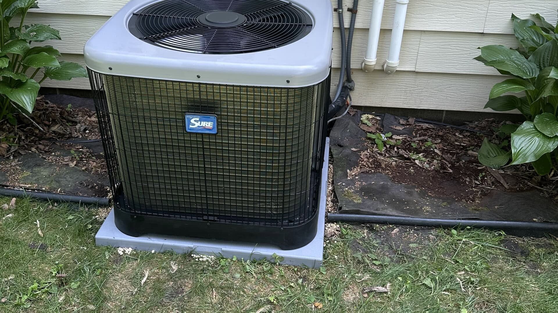 Outdoor air conditioner unit beside a house, with a black front grille and top fan.
