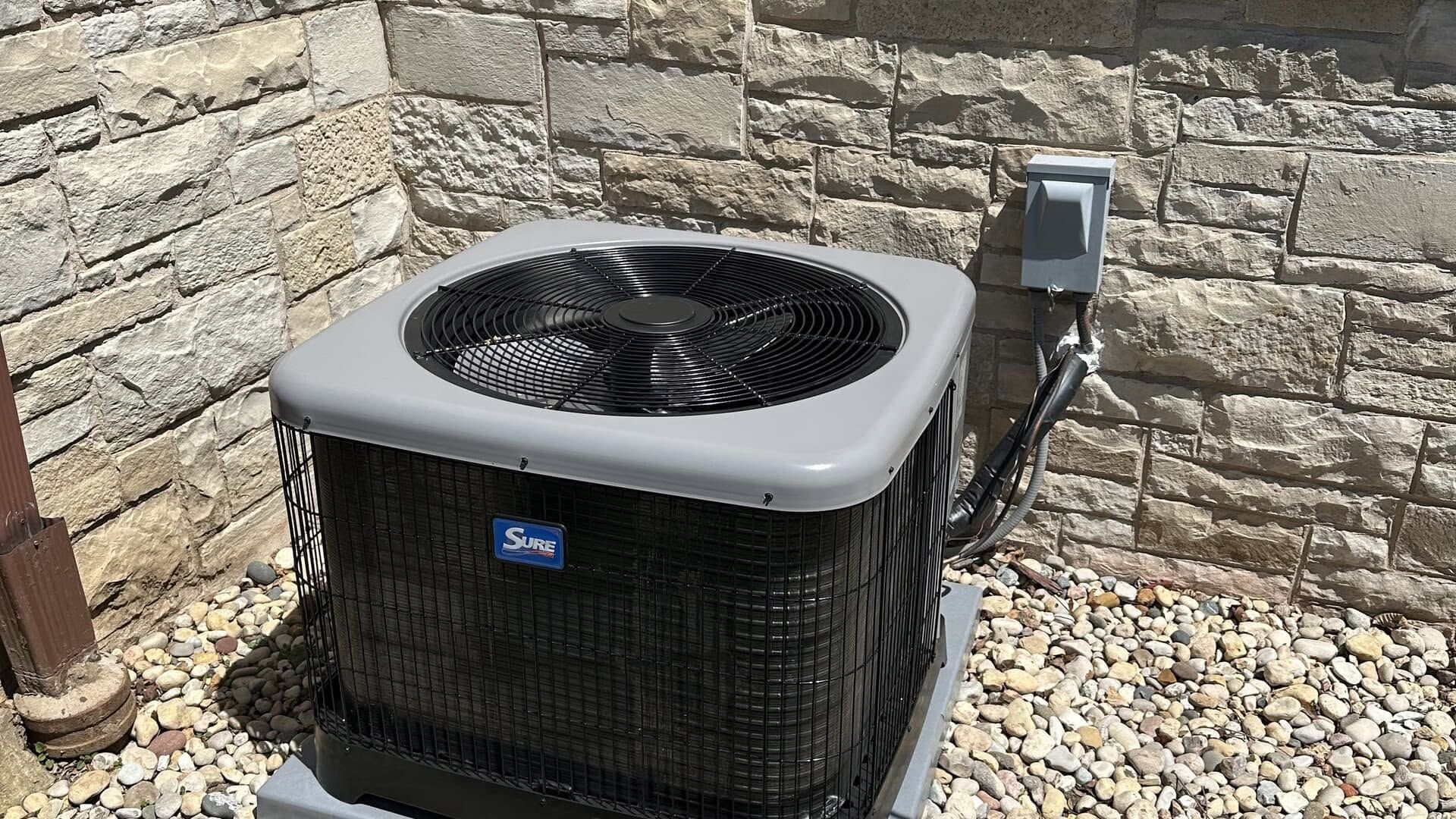 Outdoor HVAC air conditioner unit beside a stone wall and gravel ground