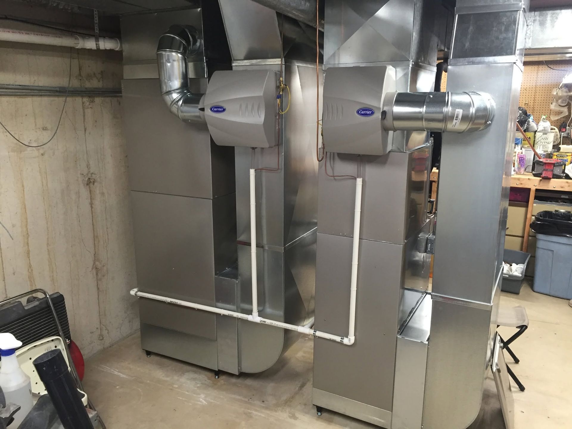 Metal ductwork and HVAC units in a basement utility room, with stainless steel piping and vents.