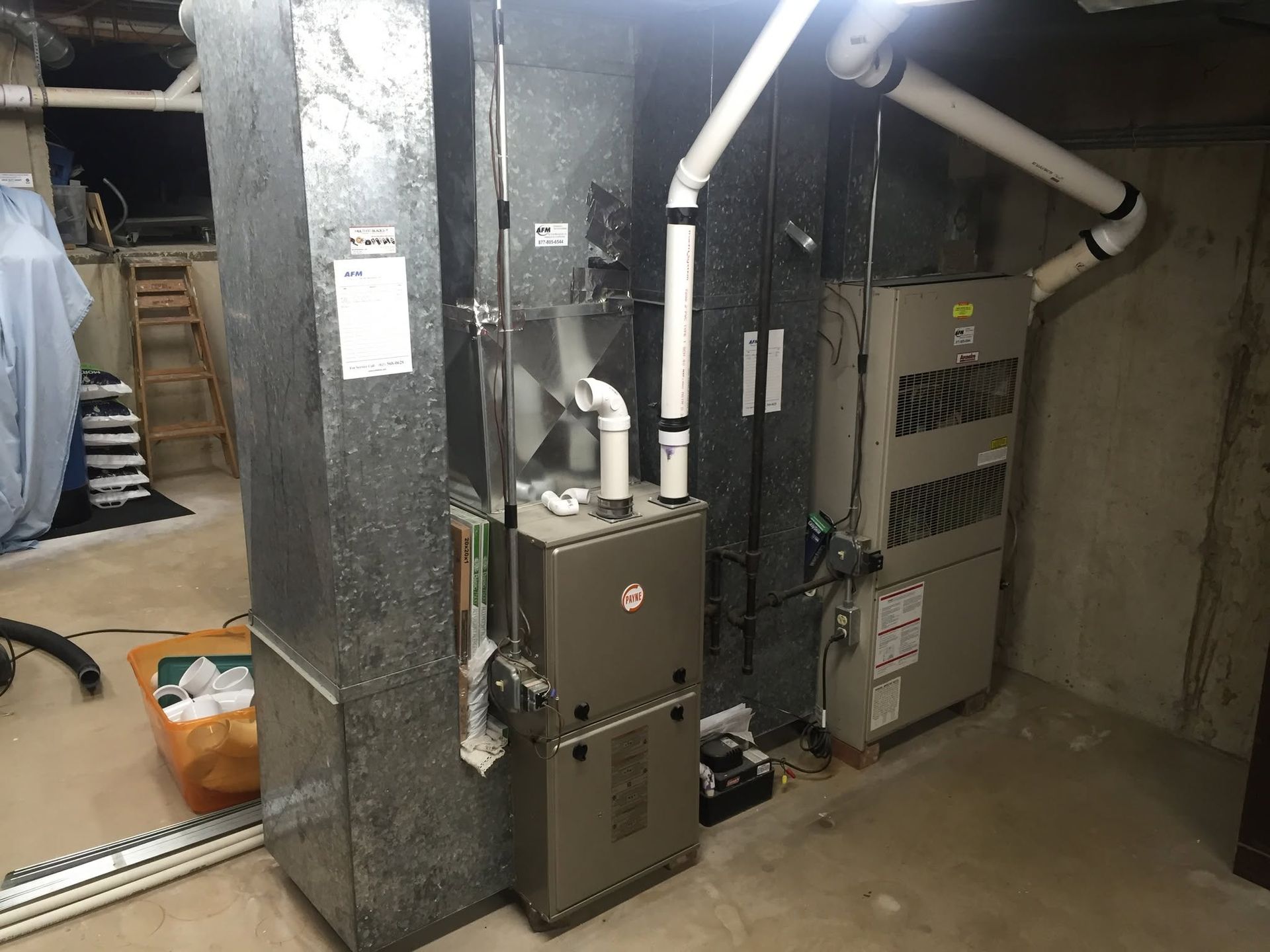 Basement utility area with furnace, water heater, and exposed pipes beside a concrete wall