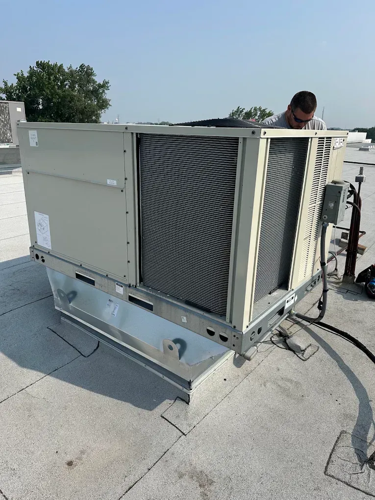 Outdoor rooftop HVAC unit with open side panel and a technician inspecting it