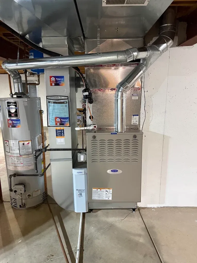 Basement furnace and HVAC equipment with exposed ductwork and utility panels on a concrete floor.
