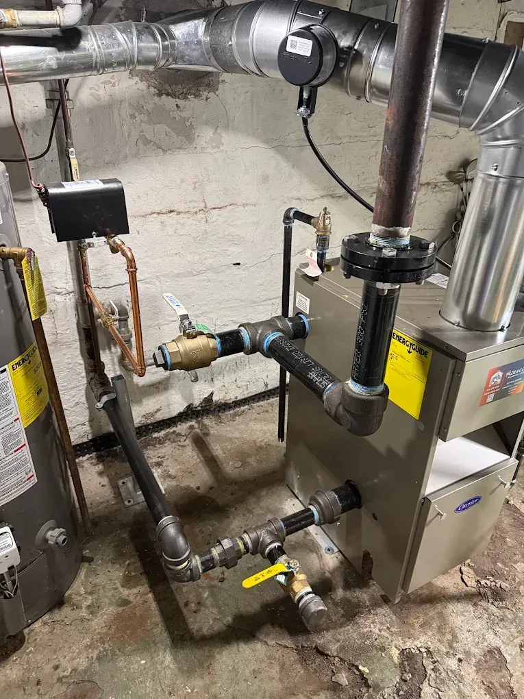 Basement boiler and pipe plumbing with valves and ductwork against a concrete wall