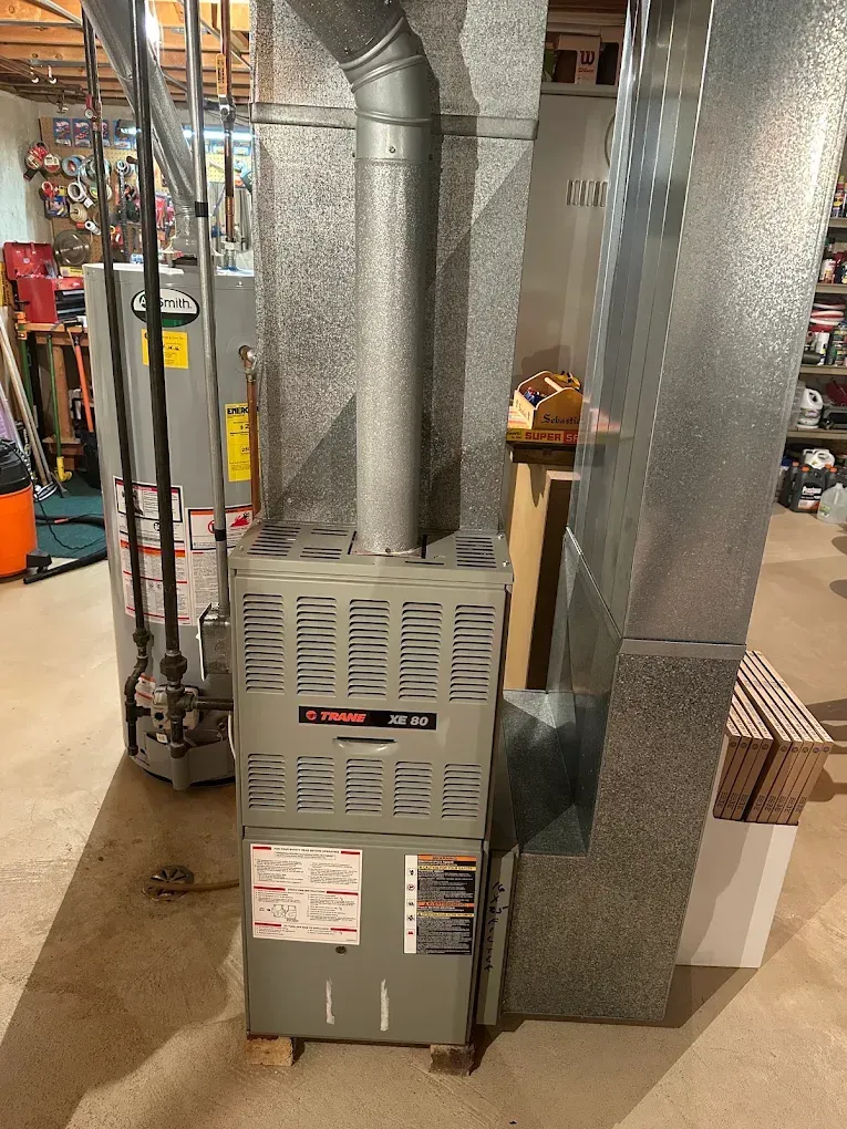 Basement furnace and HVAC ductwork in a utility room, with metal vents and pipes.