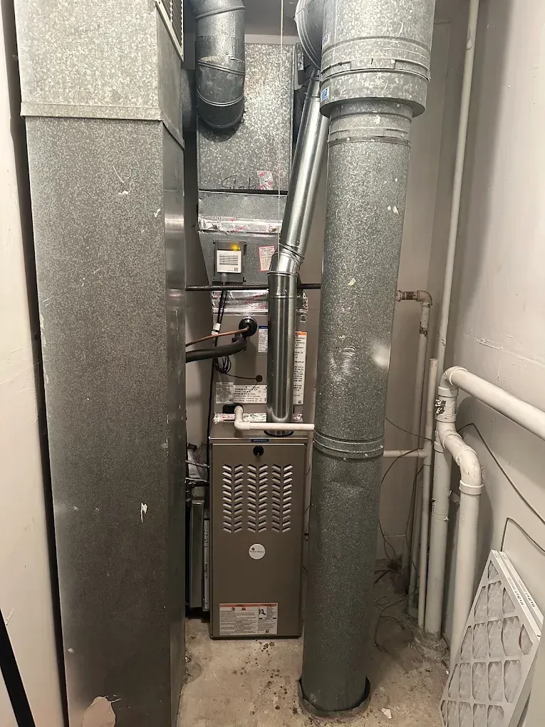 Basement HVAC furnace with ductwork, pipes, and a water heater in a narrow utility space