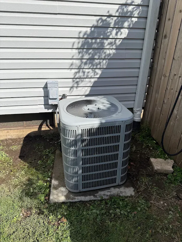 Outdoor air conditioner unit beside a house, on a concrete pad near a wall and fence.