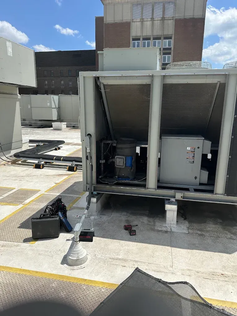 Rooftop HVAC units with open panels, tools on the ground, and a building in the background.