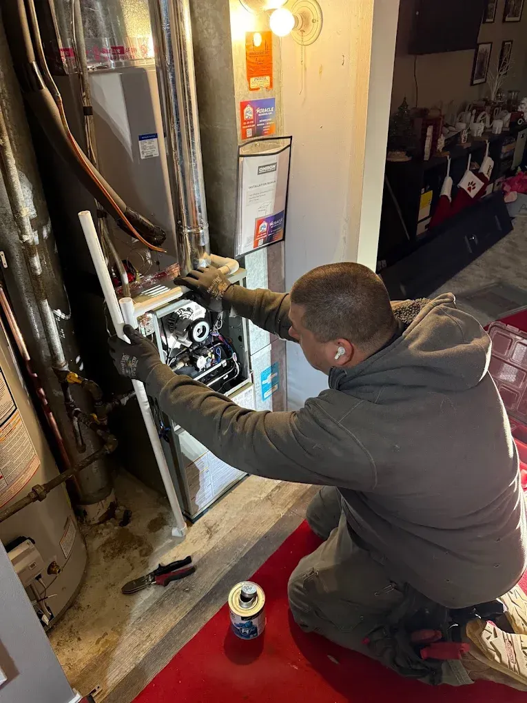 Technician kneels by an open electrical panel, adjusting wiring in a utility room with tools nearby