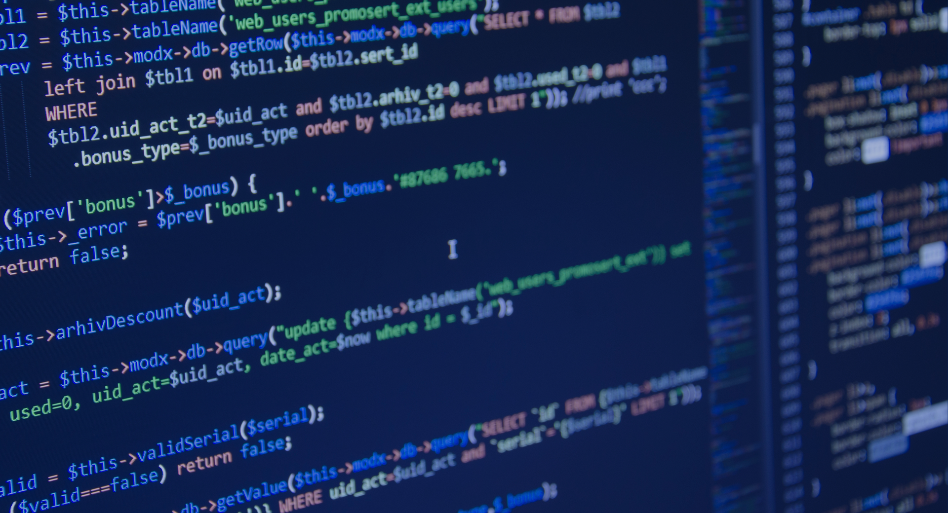 Close-up of code in blue and white on a dark computer screen, with a blurred monitor in the background