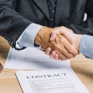 Two people shaking hands over a contract on a desk