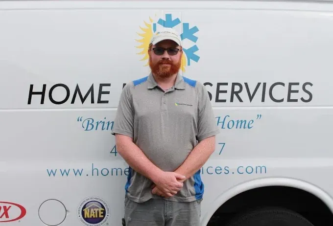 Man standing in front of a Home Services van logo, wearing sunglasses and a gray shirt.