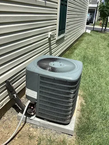 Outdoor air conditioner unit beside a house with beige siding and green lawn
