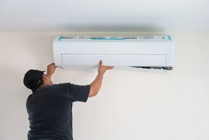 Person installing a wall-mounted air conditioner on a white wall