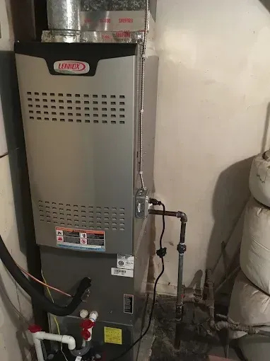 Gray furnace in a utility room with exposed pipes and ductwork, viewed from the front.