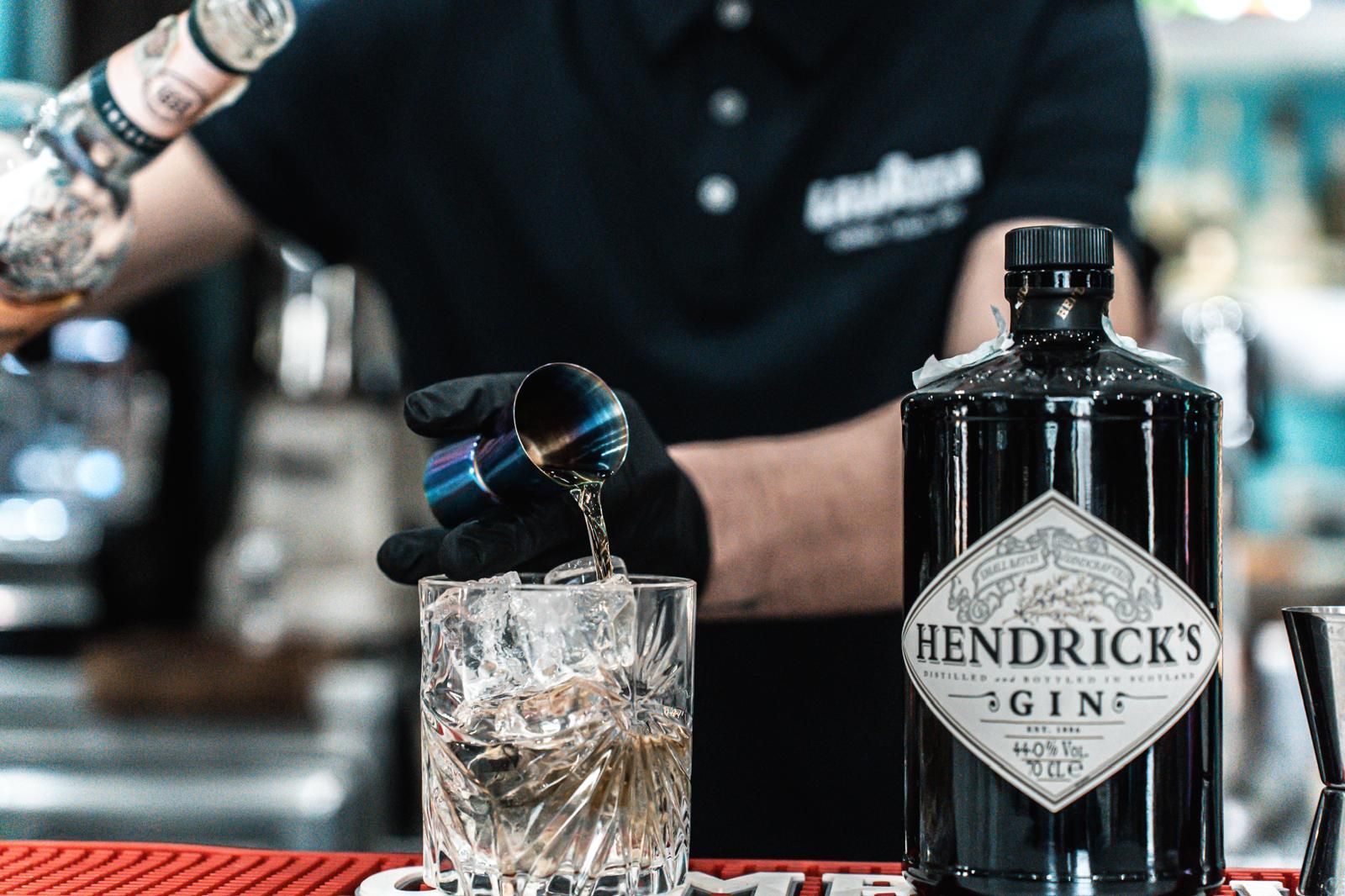 Un barista sta versando un drink in un bicchiere accanto a una bottiglia di gin Hendrick.