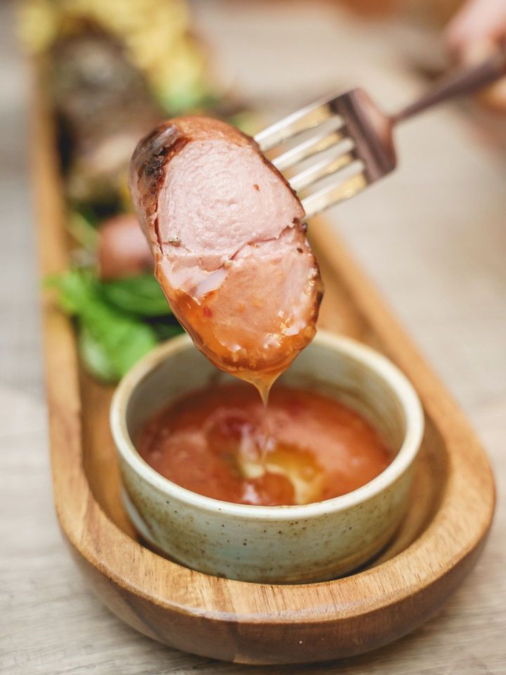 Una fetta di carne grigliata viene intinta nella salsa su un vassoio di legno con una piccola ciotola.
