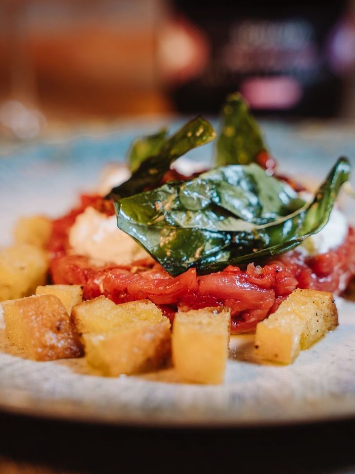 Piatto di pasta al sugo di pomodoro, formaggio grattugiato e foglie di basilico, in un primo piano all'interno di un ristorante.