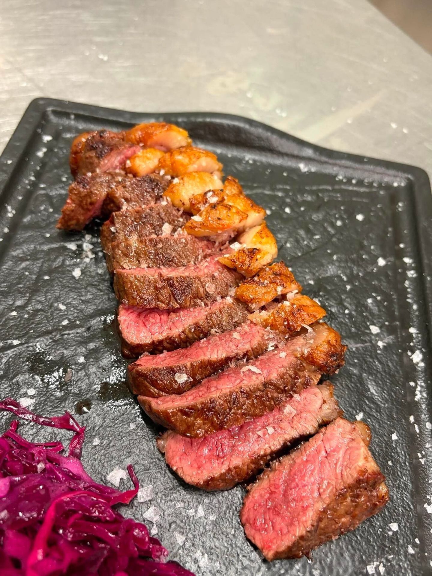Fettine di bistecca grigliata su un piatto nero con patate arrosto e cavolo rosso.