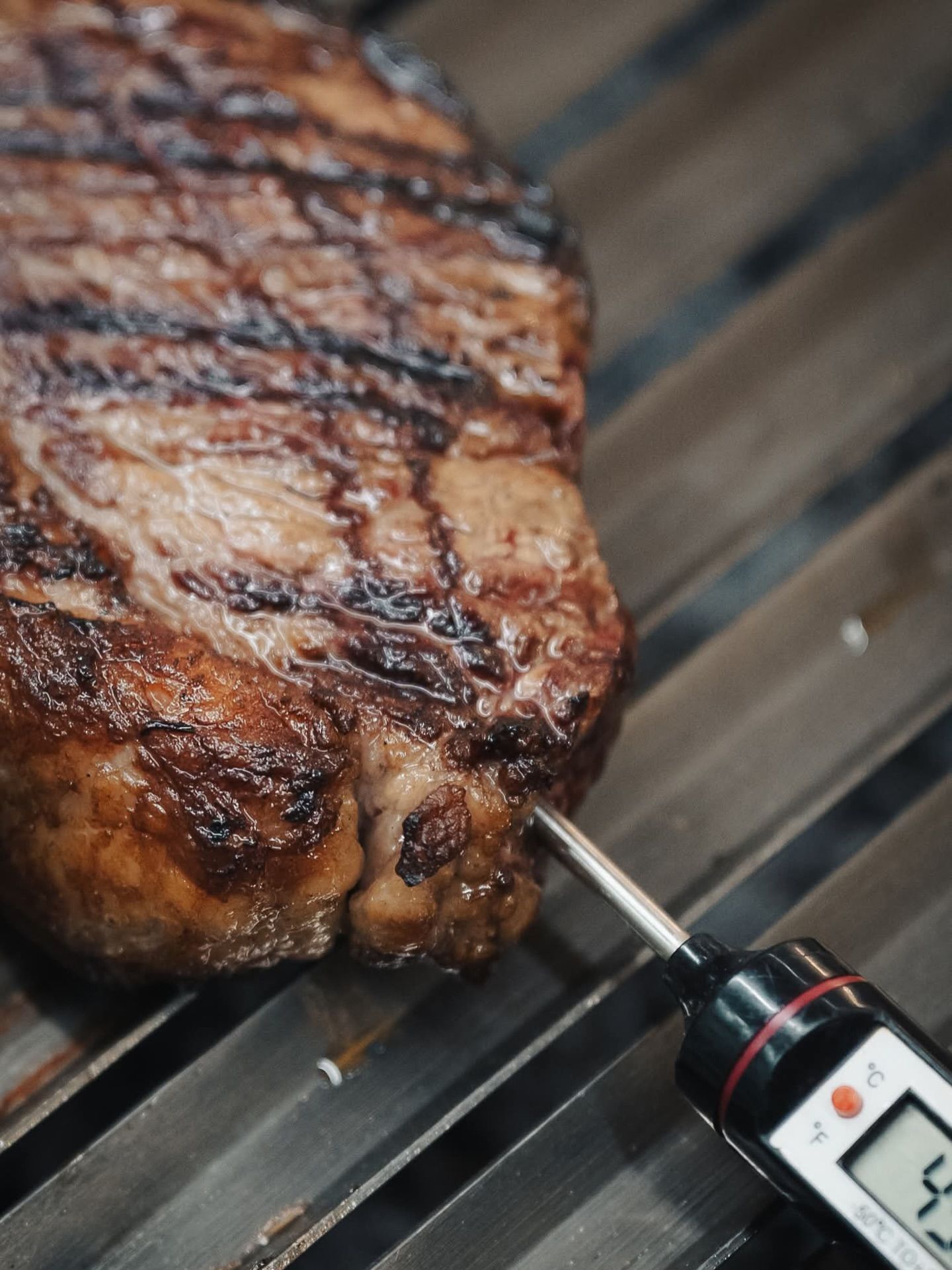 Una bistecca che cuoce sulla griglia del barbecue con un termometro per carne inserito al suo interno.