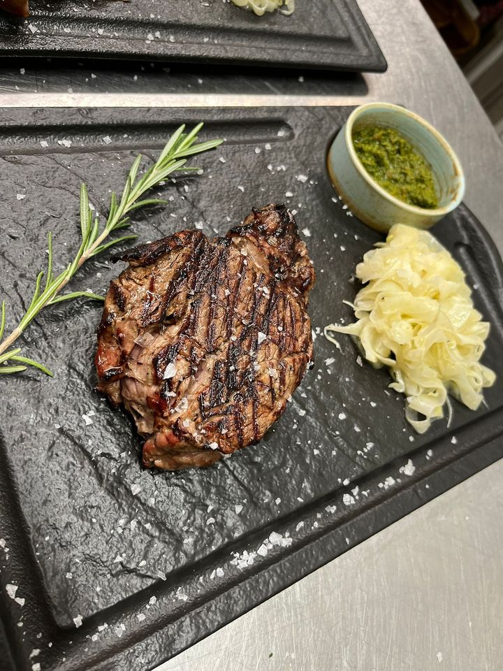 Bistecca grigliata su una lastra di ardesia nera con rosmarino, salsa verde e purè di patate come contorno.